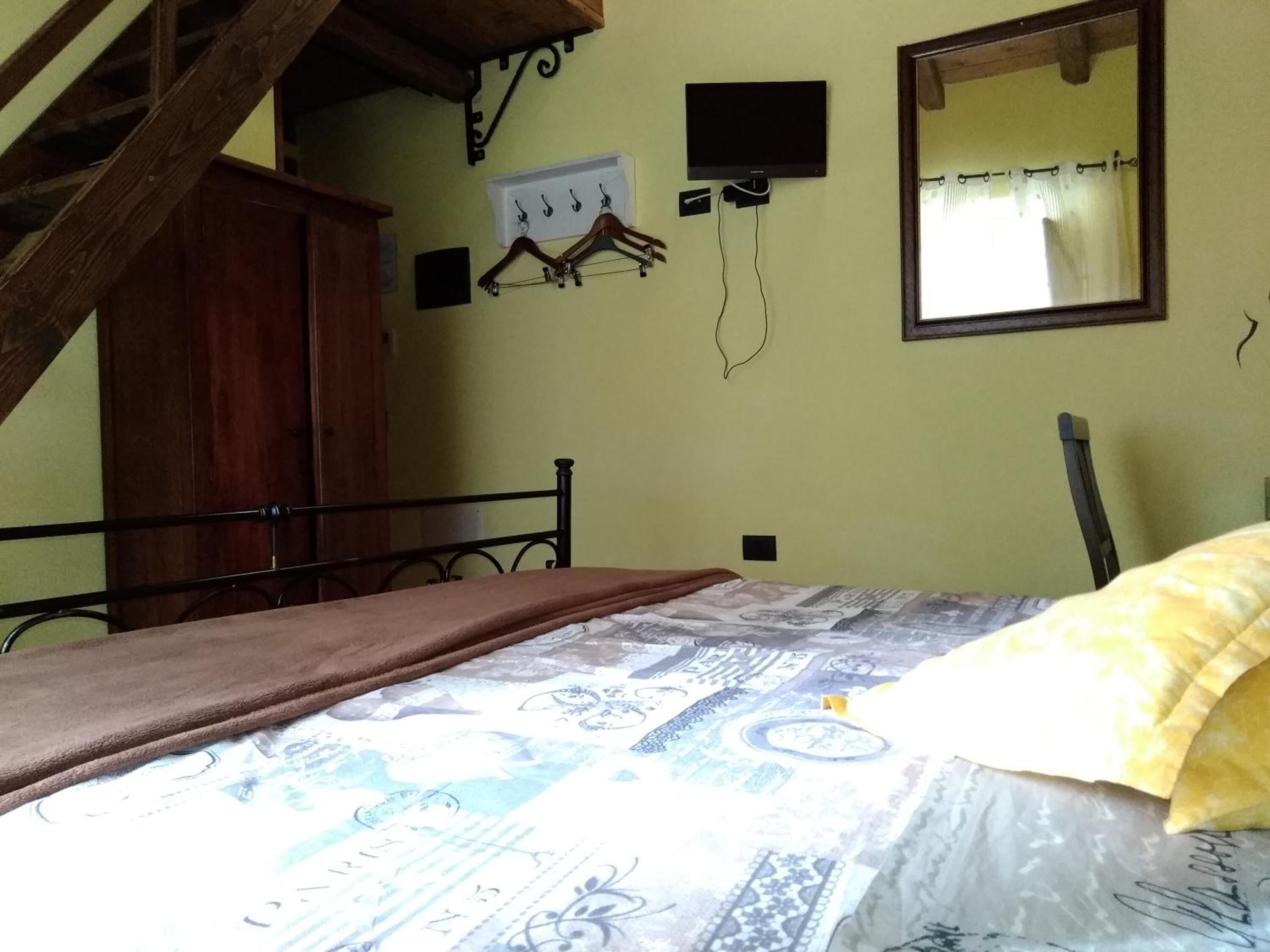 Ein Schlafzimmer mit einem Bett, einem Holzschrank, einem an der Wand befestigten Fernseher und einem Spiegel.