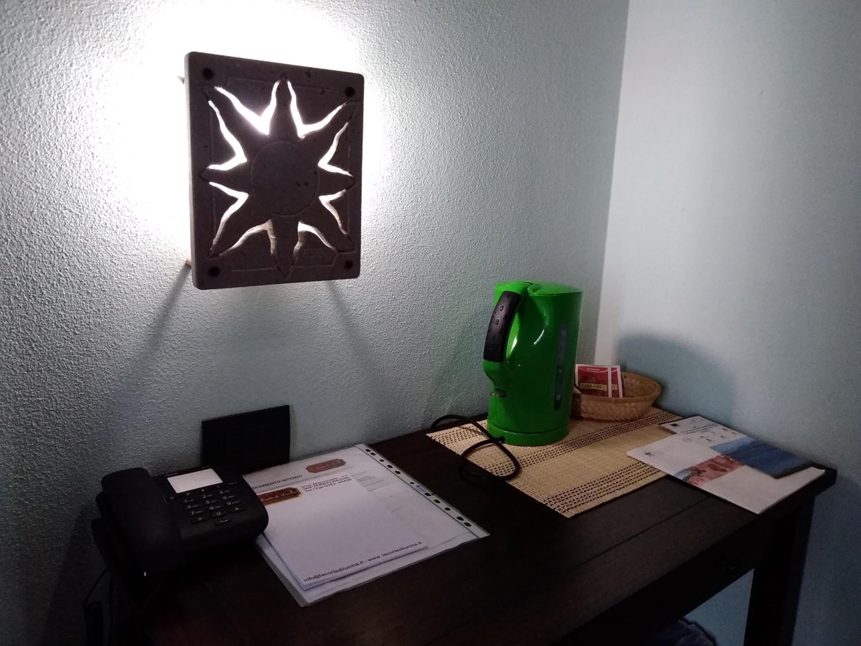 A desk with a telephone, papers, a green kettle, and a wall-mounted light fixture.