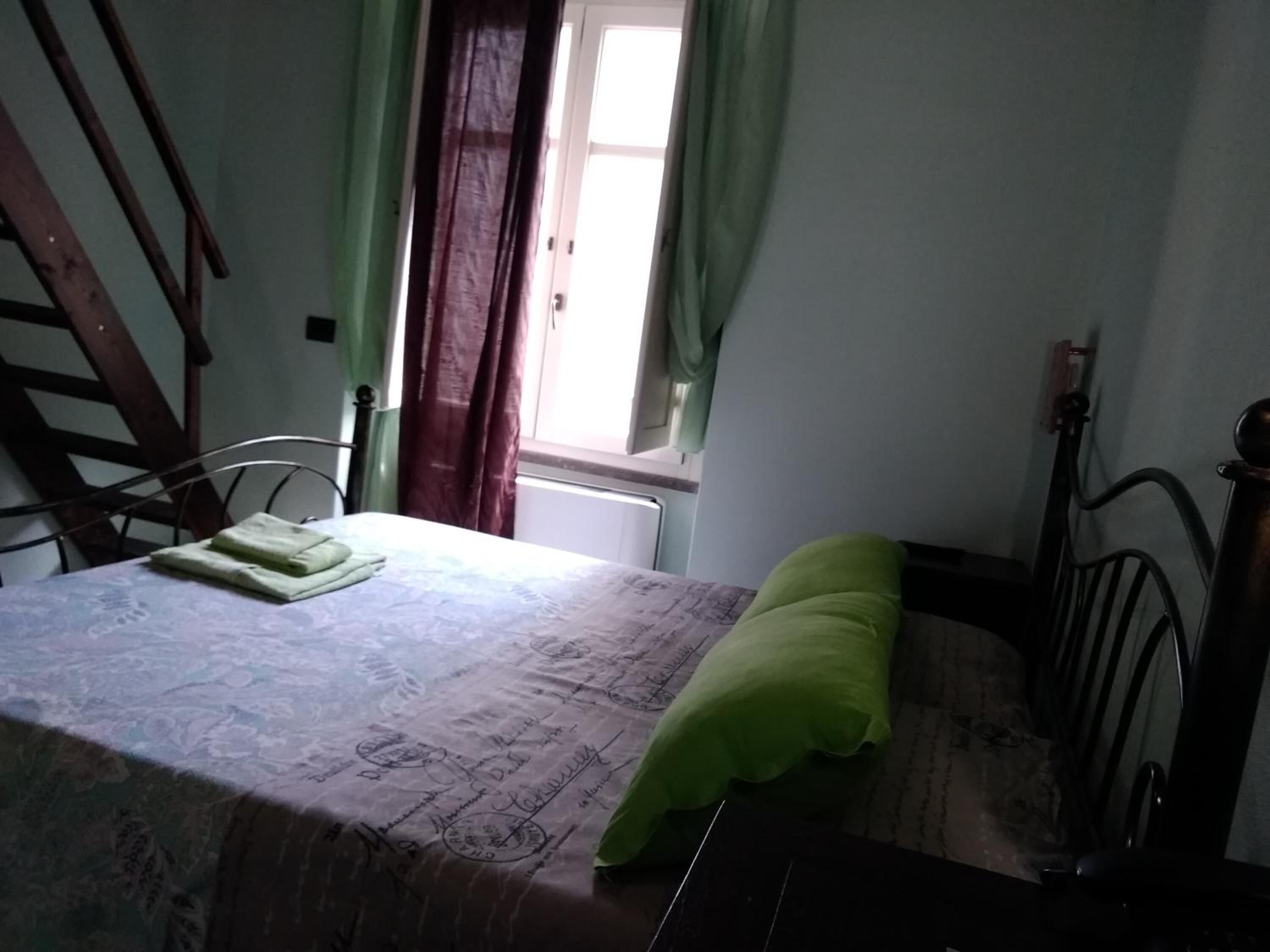 A bedroom with a bed, a chair, a window with curtains, and a radiator.