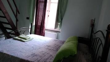 A bedroom with a bed, a chair, a window with curtains, and a radiator.