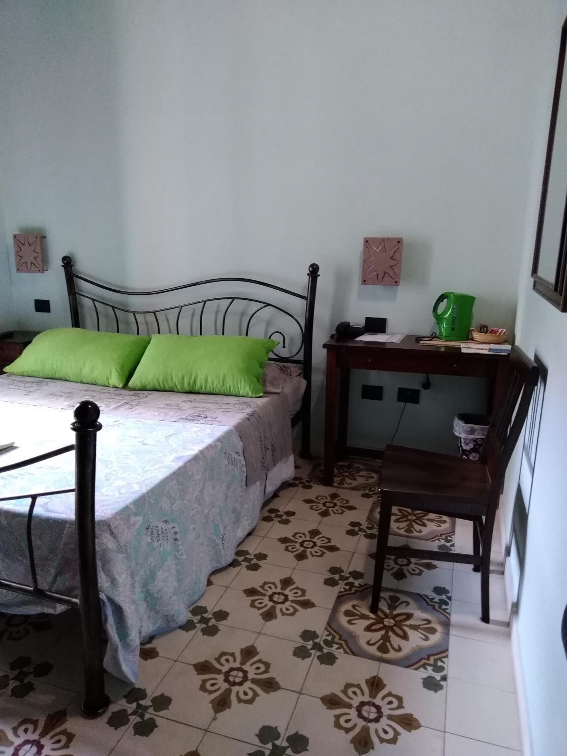 A bedroom with a bed, a nightstand, a chair, and a wall-mounted shelf.