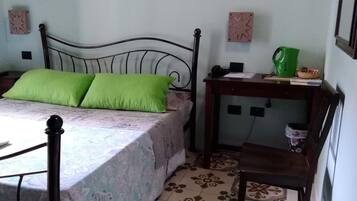 A bedroom with a bed, a nightstand, a chair, and a wall-mounted shelf.