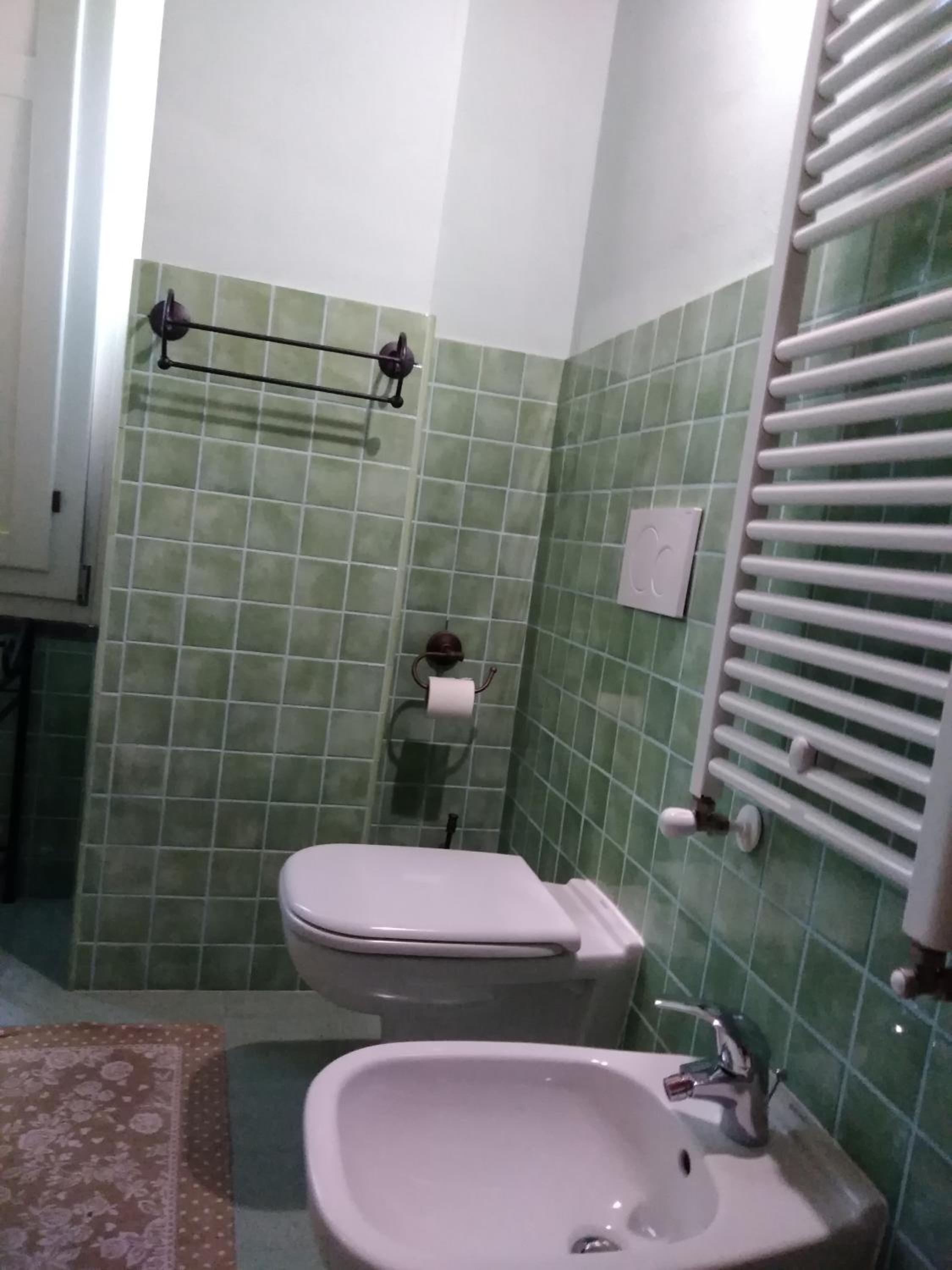 Un bagno con piastrelle verdi, un water, un lavandino e un portasciugamani.