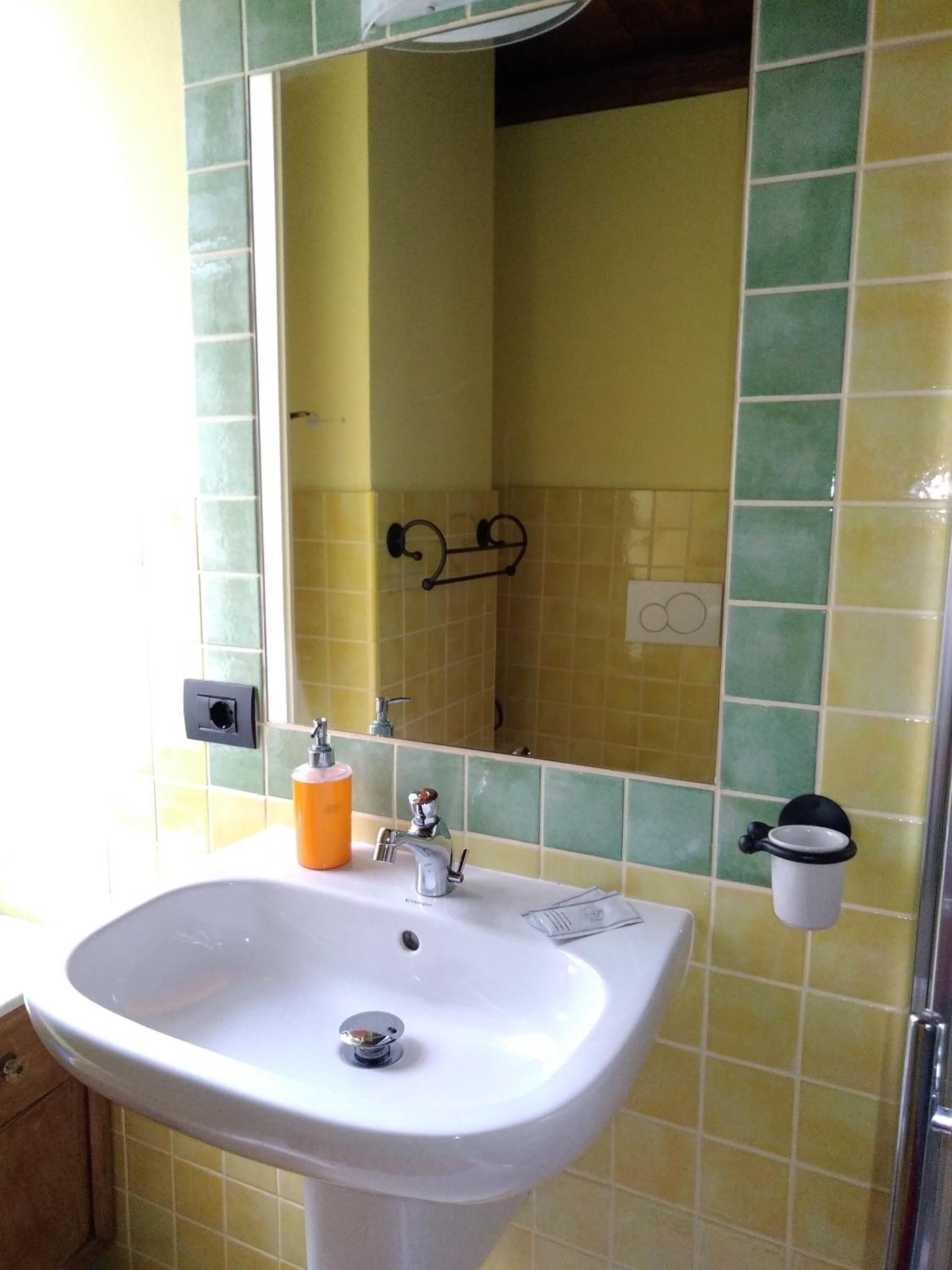 Une salle de bain avec un lavabo blanc, un miroir et des murs recouverts de carreaux jaune-vert.