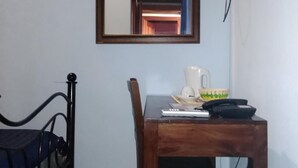 Una habitación pequeña con una cama, una mesa de madera con una taza y un plato, y un espejo en la pared.