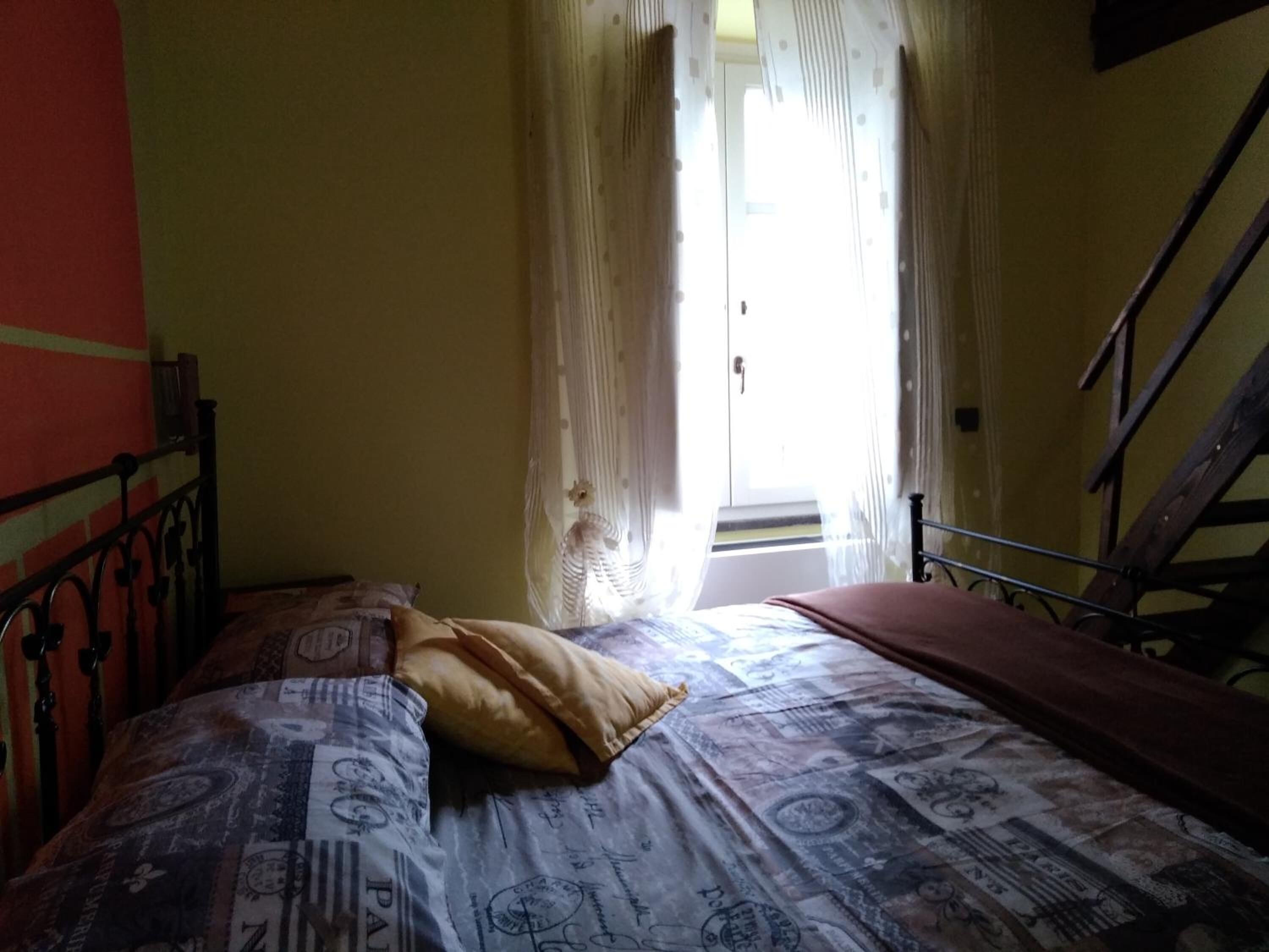 A room with a bed, a window with curtains, and a wooden staircase.