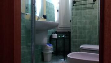 Un bagno con cabina doccia in vetro, lavandino, water e cestino.