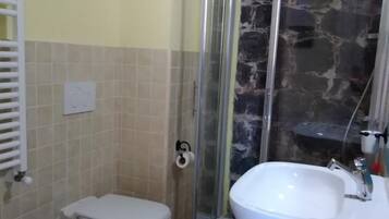 Un baño con inodoro, bidé, cabina de ducha de vidrio y lavamanos.