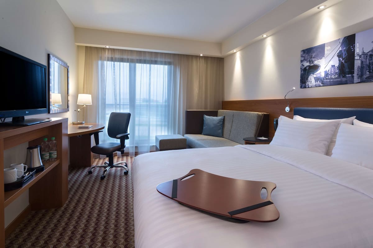 Une chambre d’hôtel comprenant un lit, un bureau avec une télévision, une chaise, un canapé et une grande fenêtre avec des rideaux.