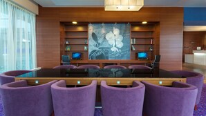 Une salle de conférence avec une table en verre, des chaises violettes, deux écrans et un grand tableau représentant une orchidée au mur.