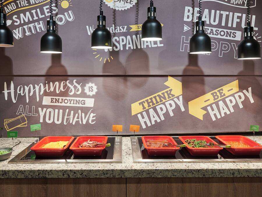 A buffet area with multiple food trays and a motivational wall with phrases like "Happiness is all you have" and "Think happy."