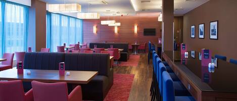 A modern restaurant with booths and tables, red and blue seating, and wooden panel walls.