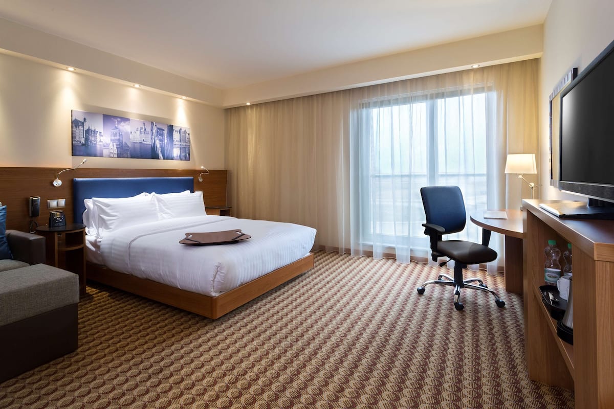 Une chambre d’hôtel avec un grand lit, un bureau avec une télévision, une chaise et un canapé.