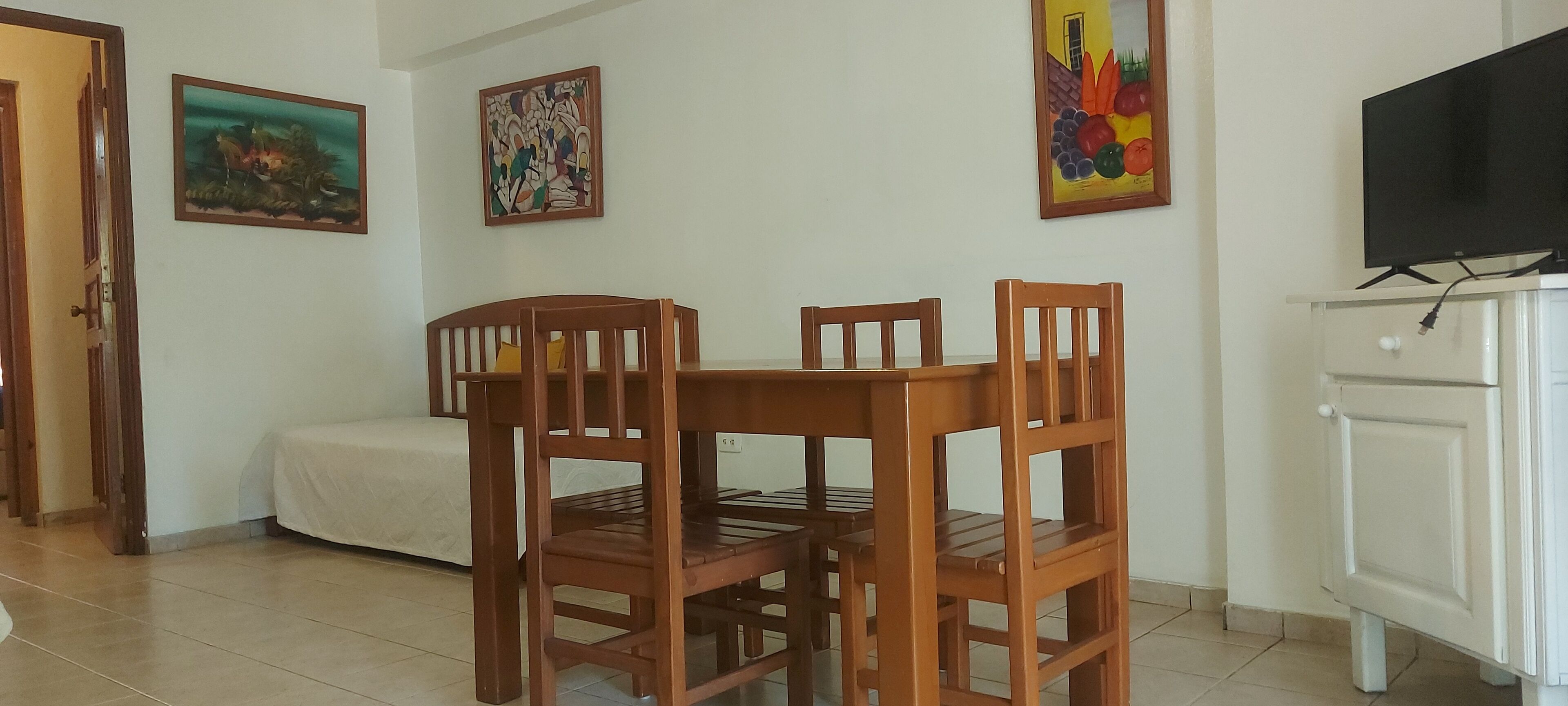 A dining area with a wooden table and chairs, a white cabinet, and a television on a stand.