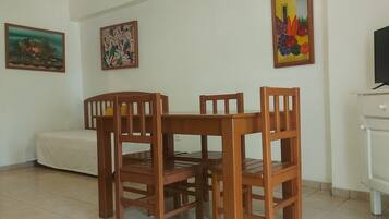 A dining area with a wooden table and chairs, a white cabinet, and a television on a stand.