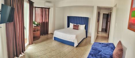 A hotel room with a bed, a TV, a desk, and a window with curtains.