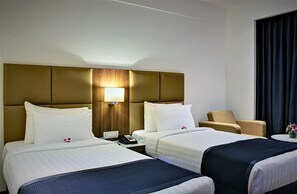 A hotel room with two beds, a wooden headboard, a bedside table with a lamp, a chair, and a small table with a vase. - Ramada Encore by Wyndham Bangalore Domlur (Bengaluru)
