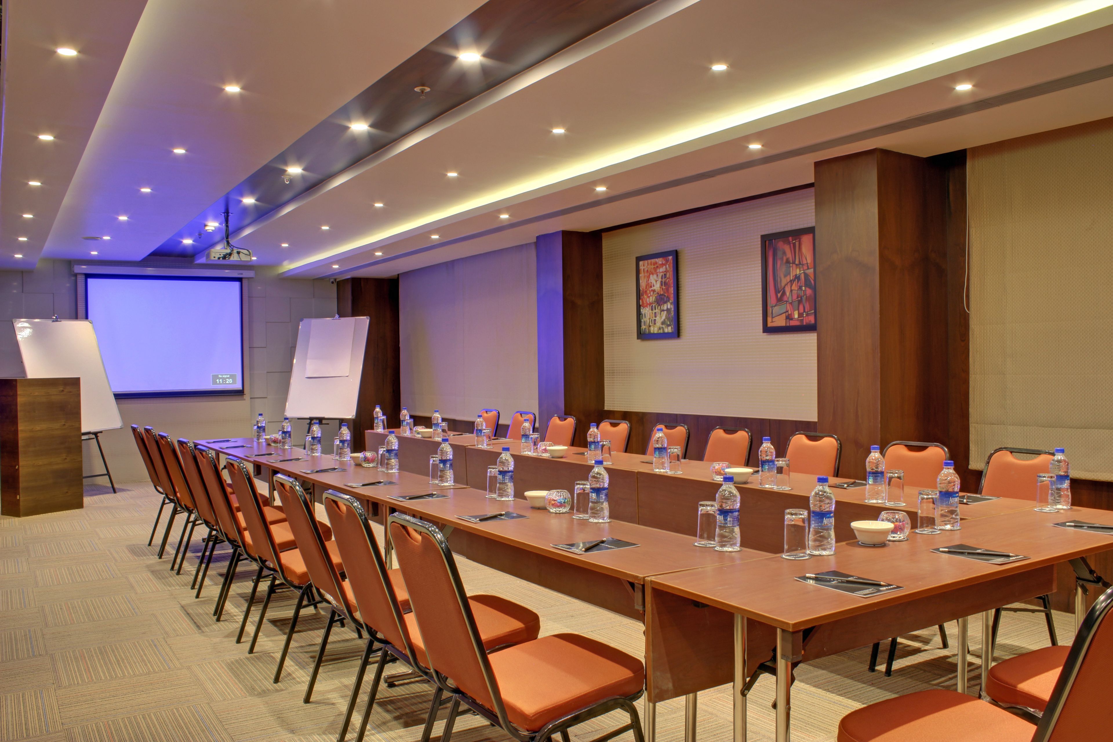 A conference room with a long table, chairs, water bottles, and a projector screen.