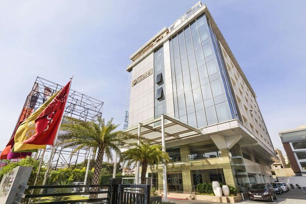 A modern hotel with a glass facade, a prominent entrance, and a parking area with cars. - Ramada Encore by Wyndham Bangalore Domlur (Bengaluru)