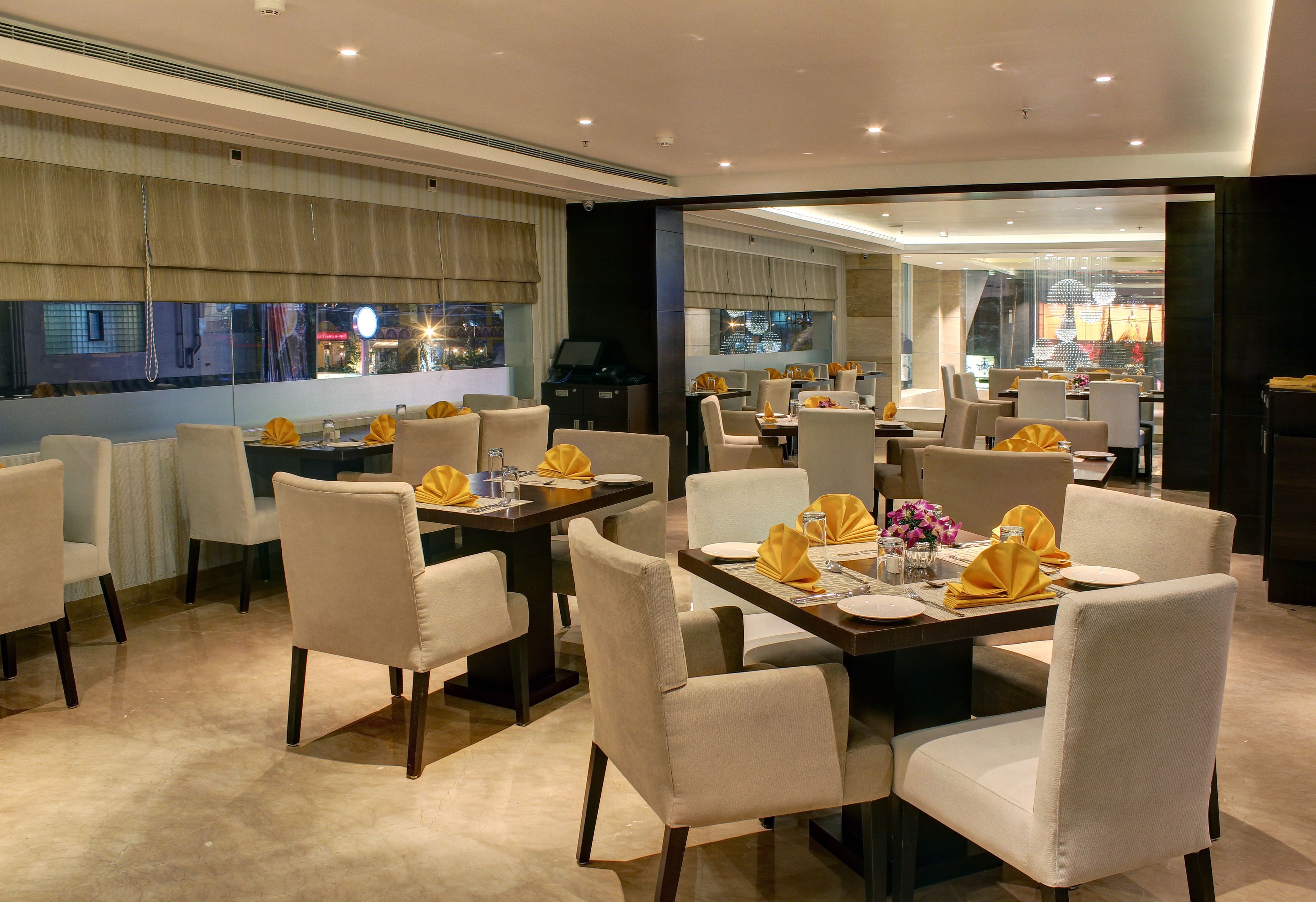 A modern dining area with tables set for four, each with white chairs and yellow napkins.