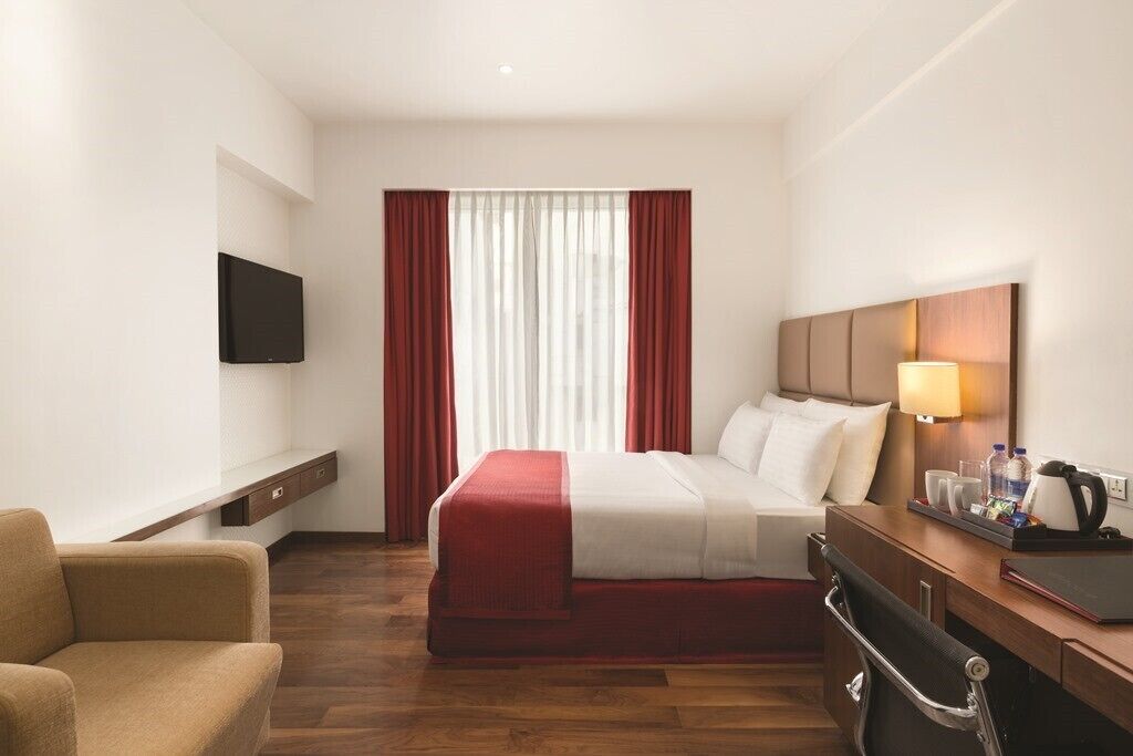 A hotel room with a bed, a desk, a chair, a TV, and a window with curtains.