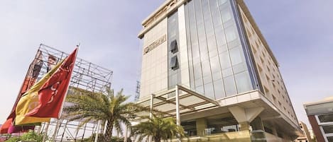 Un hotel moderno con fachada de vidrio, una entrada destacada y un estacionamiento con coches.