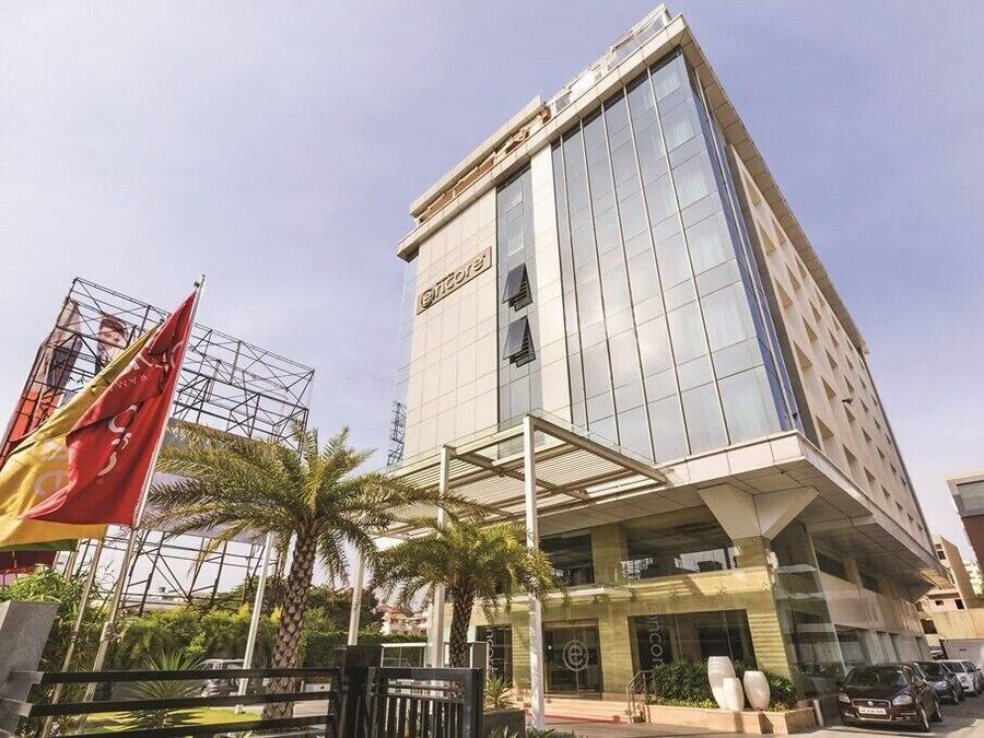 A modern hotel with a glass facade, a prominent entrance, and a parking area with cars.