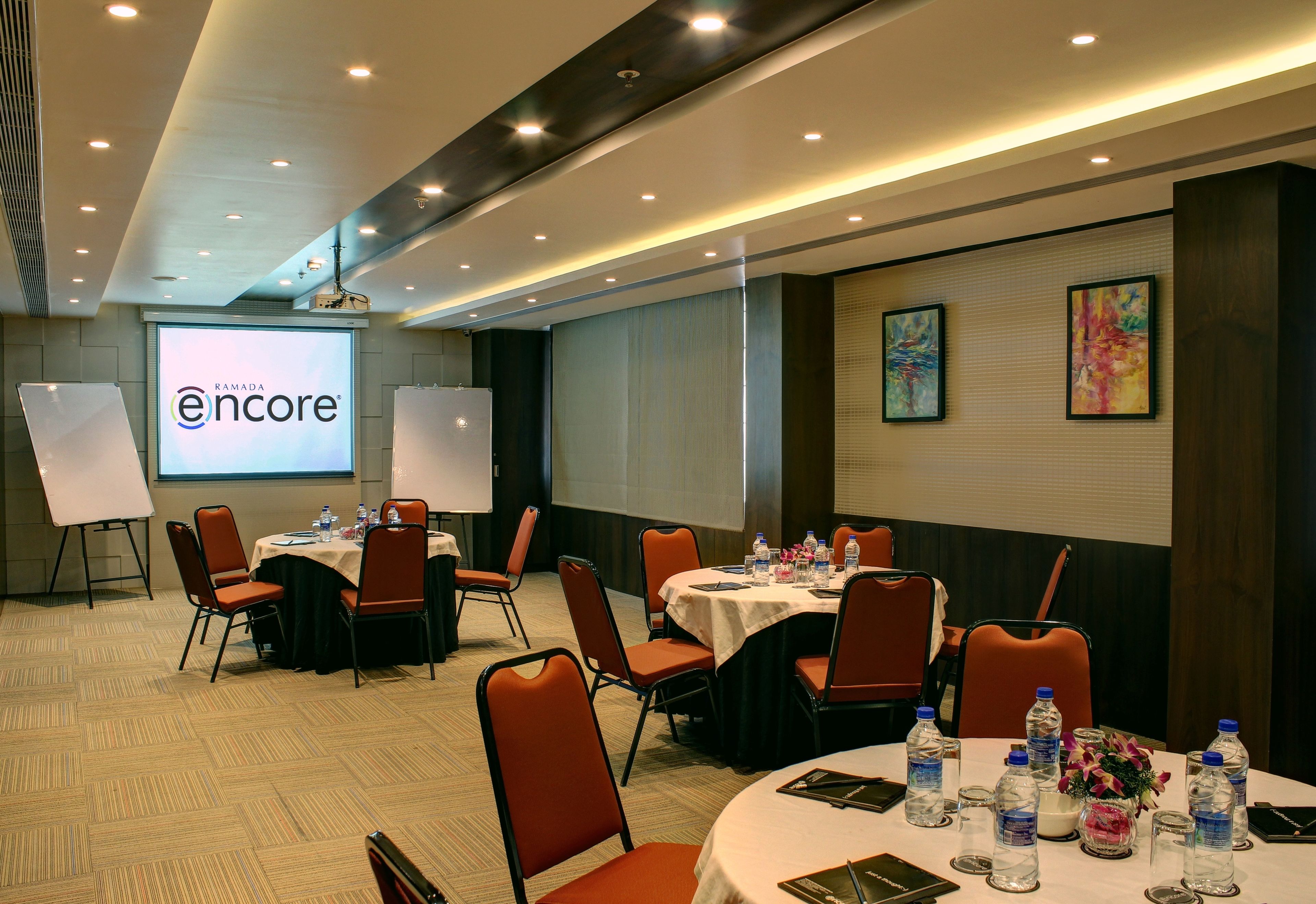 A conference room with multiple tables, chairs, and presentation screens.