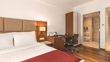 Habitación de hotel con cama, escritorio, silla y baño visible a través de una puerta abierta.