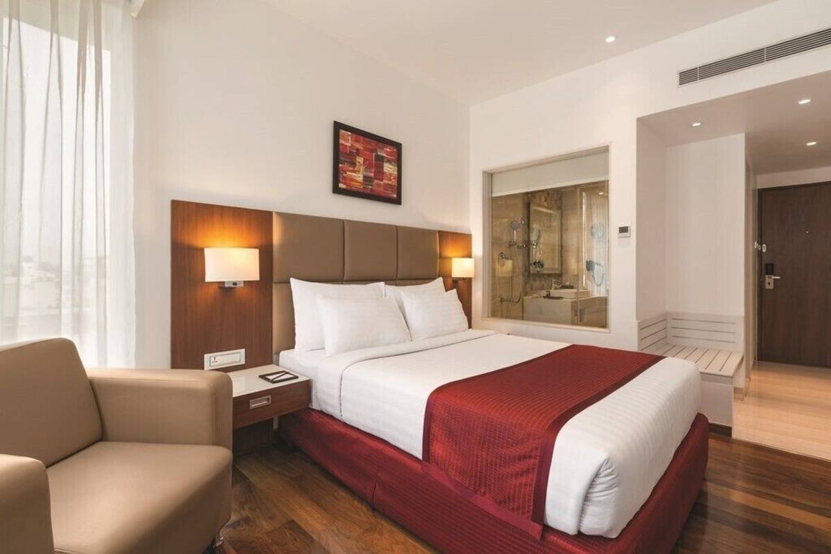 Een hotelkamer met een groot bed, een bureau met stoel, een nachtkastje, een spiegel en een raam met gordijnen.