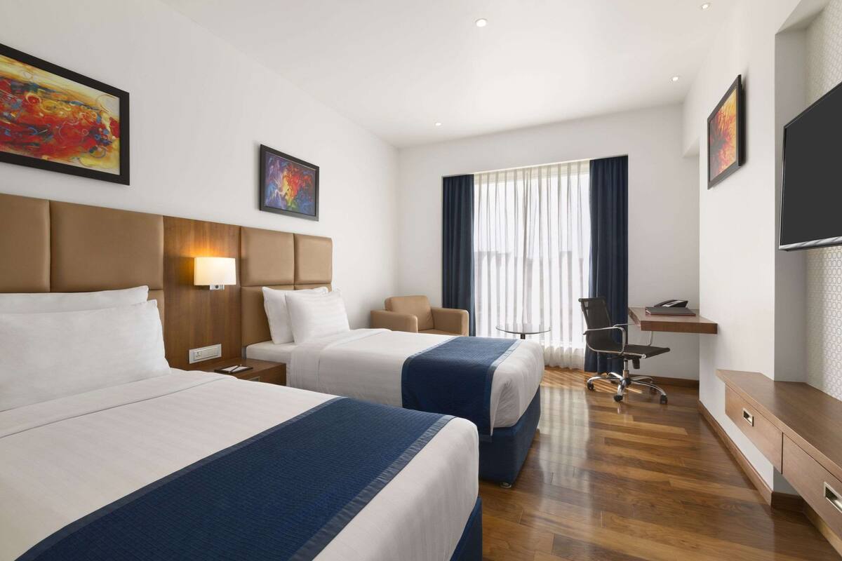 Een hotelkamer met twee bedden, een bureau, een stoel en een televisie.