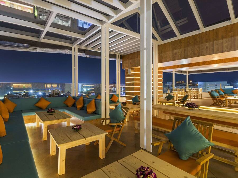 Un salón tipo loft con asientos y mesas, ventanas amplias y vistas a la ciudad iluminada de noche.