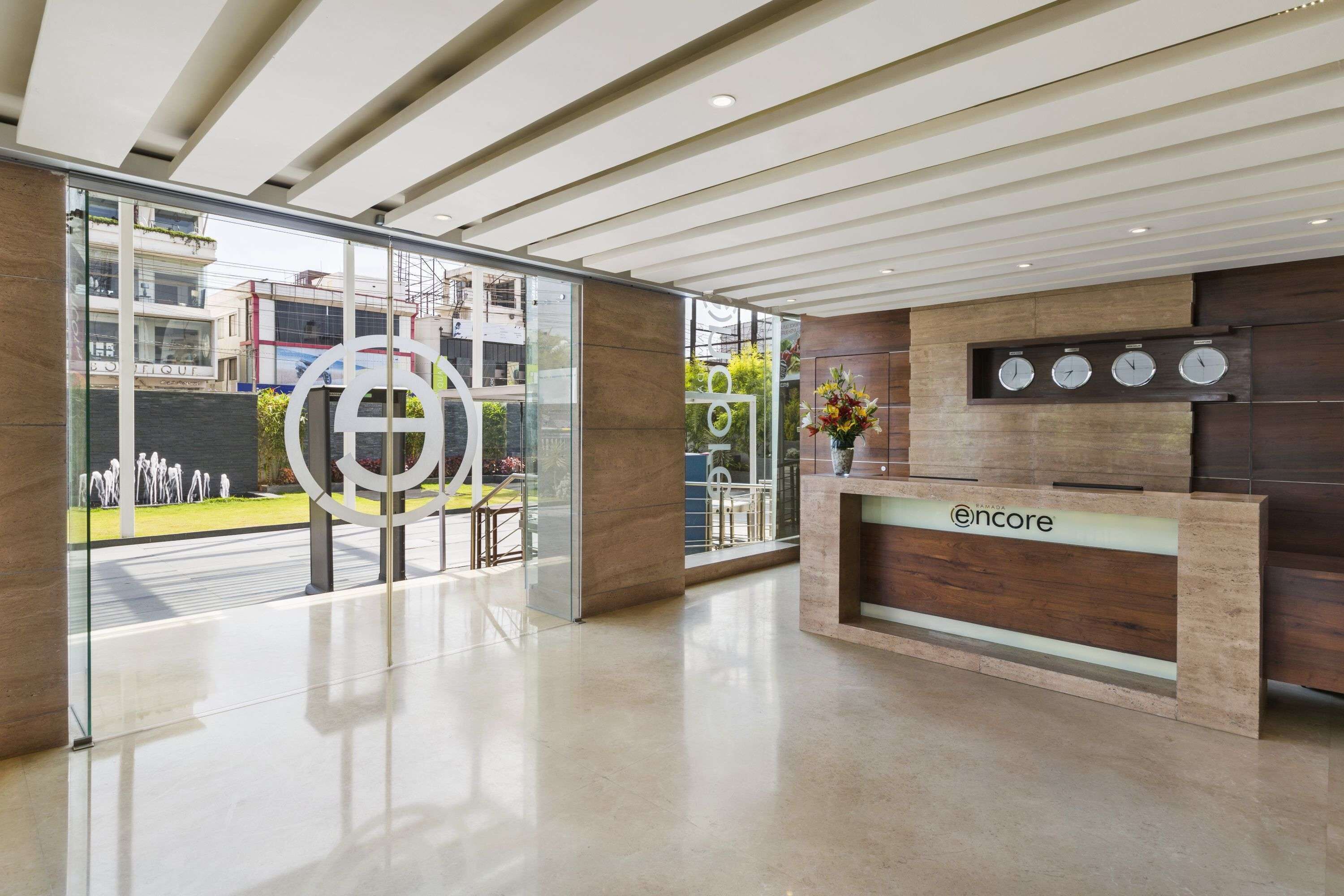 Un área de recepción moderna con un panel de vidrio, un mostrador de recepción y una pantalla de reloj digital.
