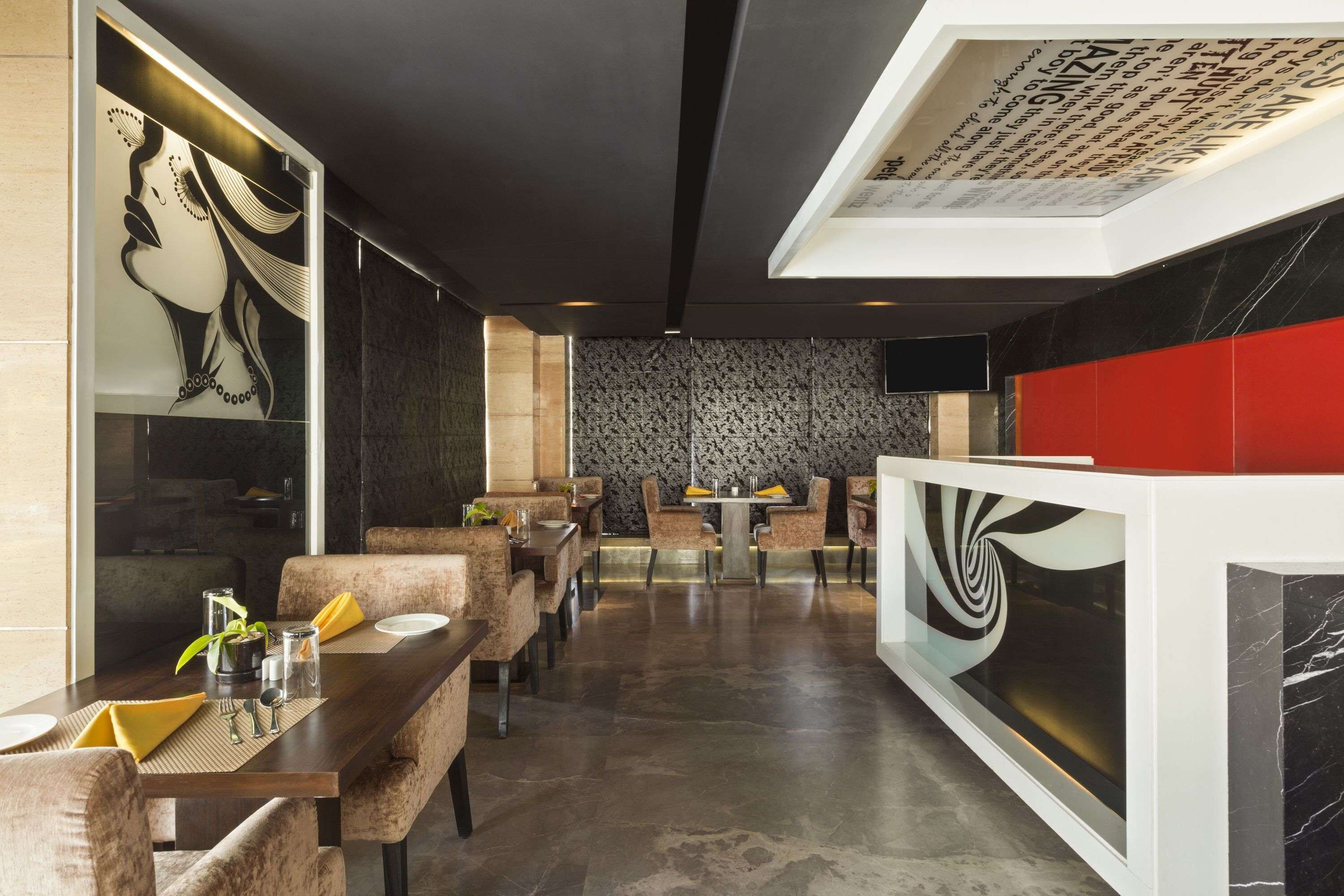 A modern restaurant interior with a long dining table, cushioned chairs, and a patterned wall.