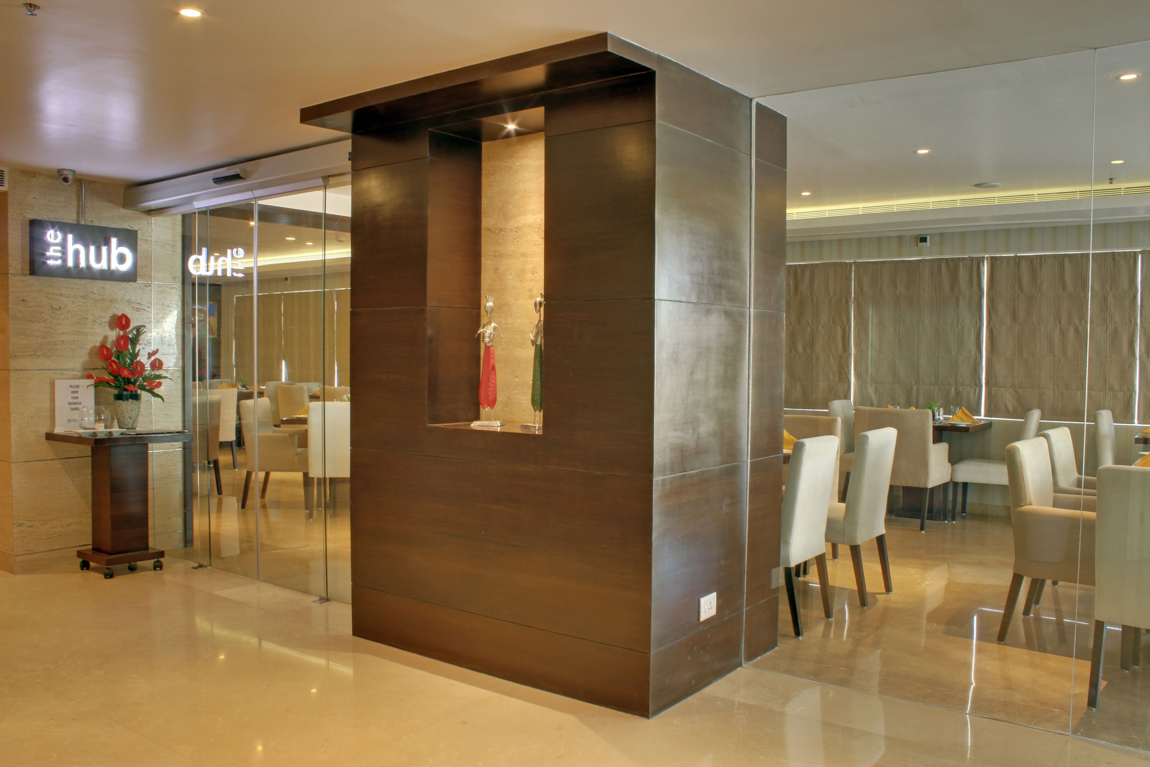 Un moderno vestíbulo de hotel con un mostrador de recepción, un separador de vidrio y una zona de estar con sillas y mesas.