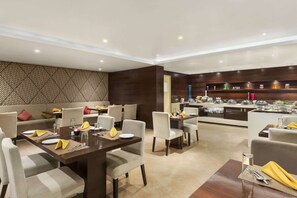 A modern dining area with a central table, surrounded by sofas and chairs, and a kitchen area with buffet setup. - Ramada Encore by Wyndham Bangalore Domlur (Bengaluru)