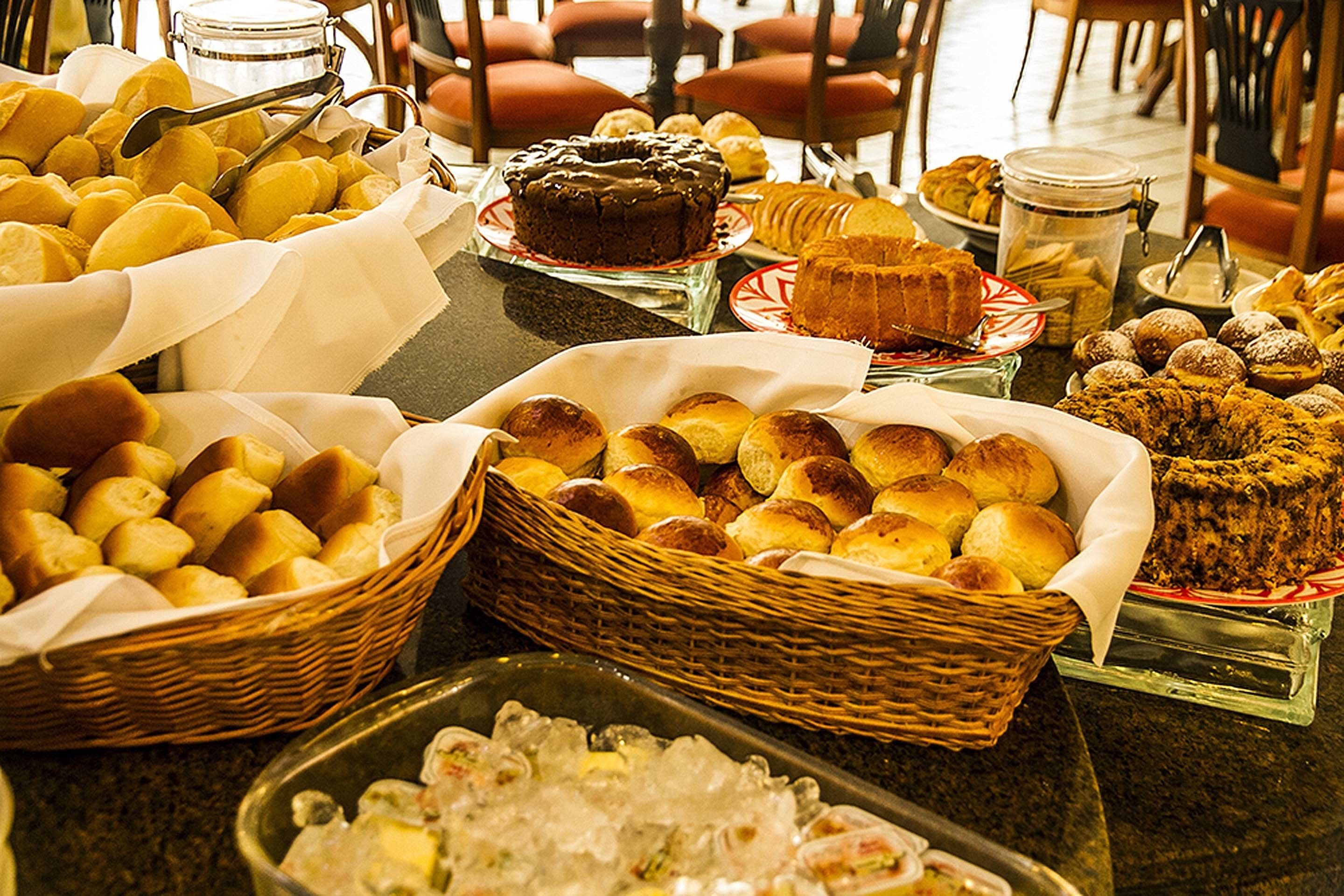 Uma mesa de buffet com diversos pães e sobremesas.
