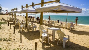 A beachside restaurant with outdoor seating, including plastic chairs and tables, under wooden umbrellas. - Resort Arcobaleno All Inclusive (Porto Seguro)