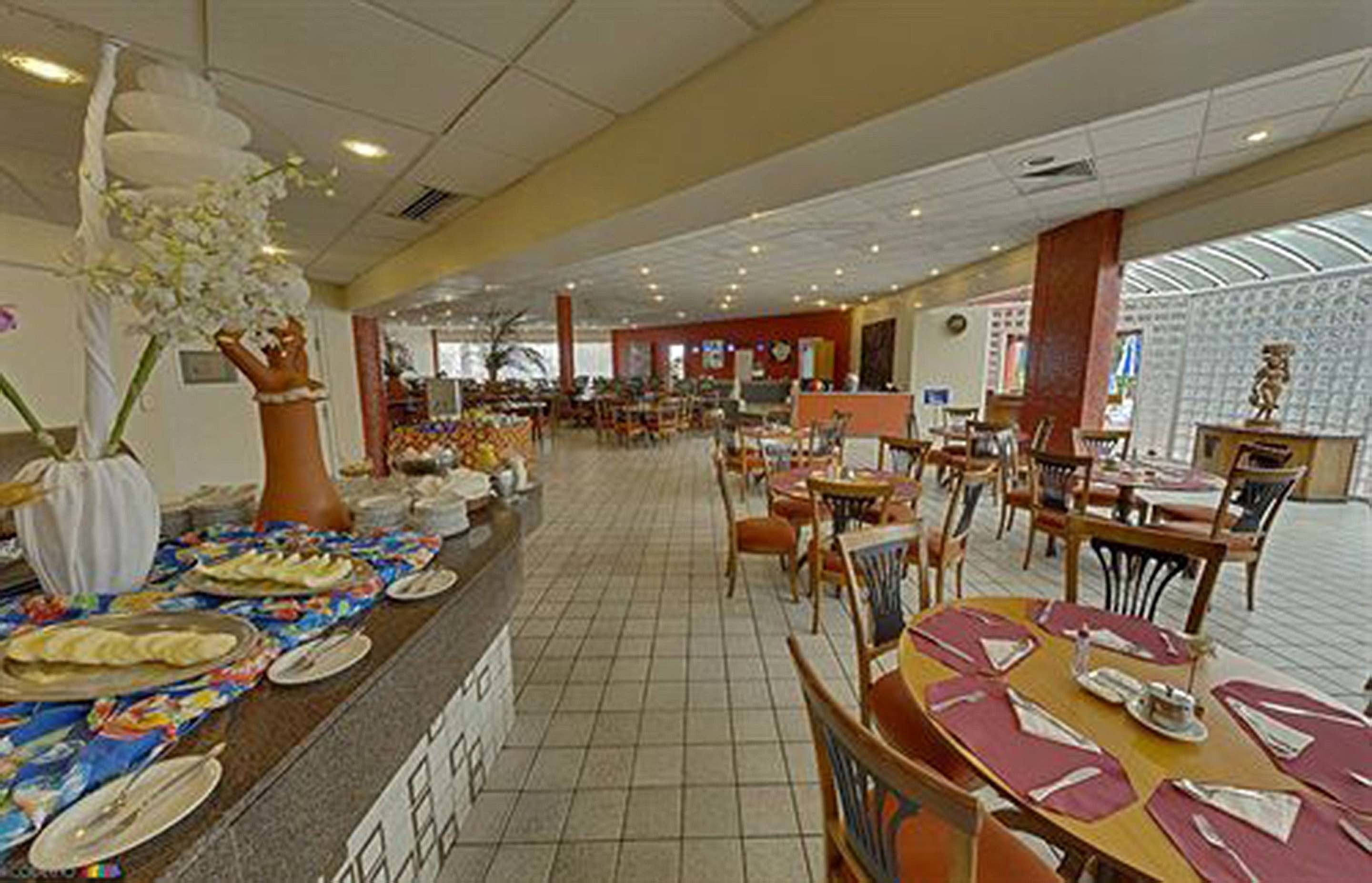 Un comedor amplio con varias mesas y sillas, una barra de servicio central y una orquídea blanca decorativa.