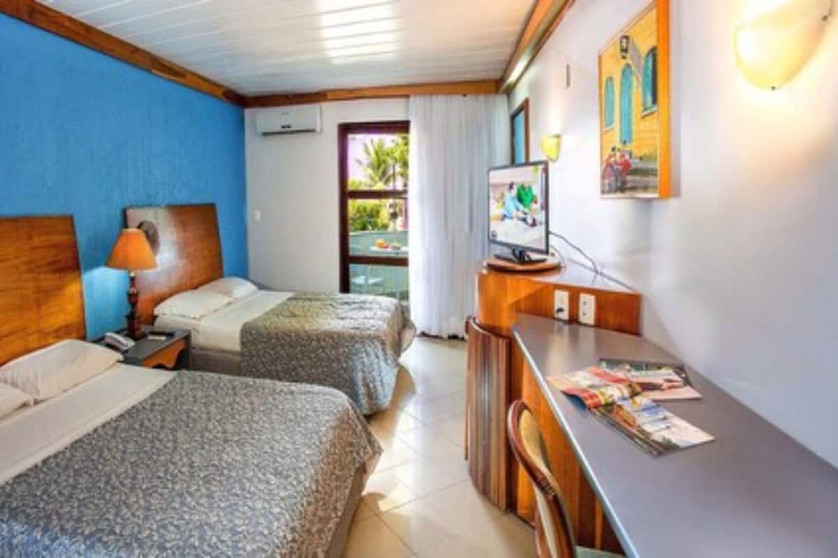 A hotel room with two beds, a desk, a TV, and a window with curtains.
