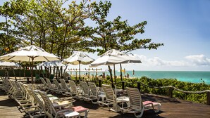 A wooden deck with white lounge chairs and umbrellas, overlooking a beach and ocean. - Resort Arcobaleno All Inclusive (Porto Seguro)