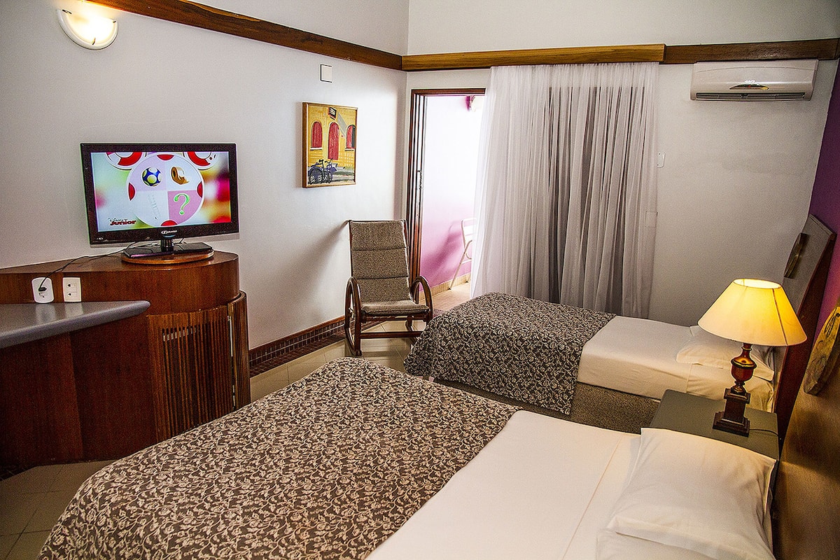 A hotel room with two beds, a television, a chair, and a window with curtains.