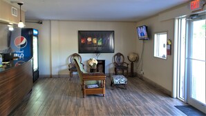 A lobby with a reception desk, seating area, television, and a large window. - Eastern Shore Motel (Daphne)