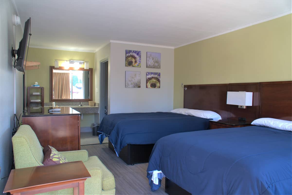 Una habitación de hotel con dos camas, un escritorio, una silla, un televisor y obras de arte en la pared.
