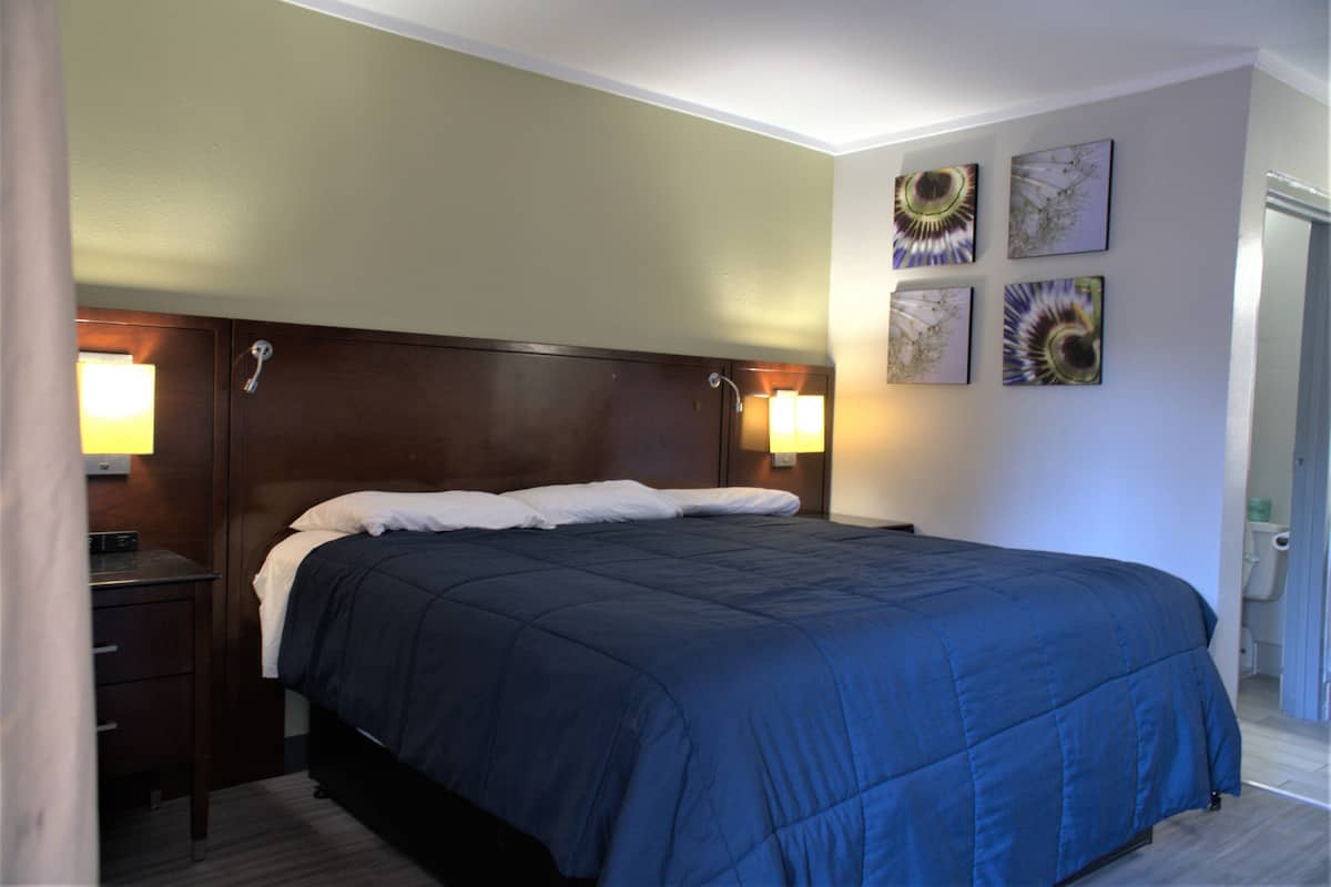 Una cama bien hecha con un edredón azul oscuro y almohadas blancas, un cabecero de madera, dos lámparas de noche y cuatro obras de arte colgadas en la pared.
