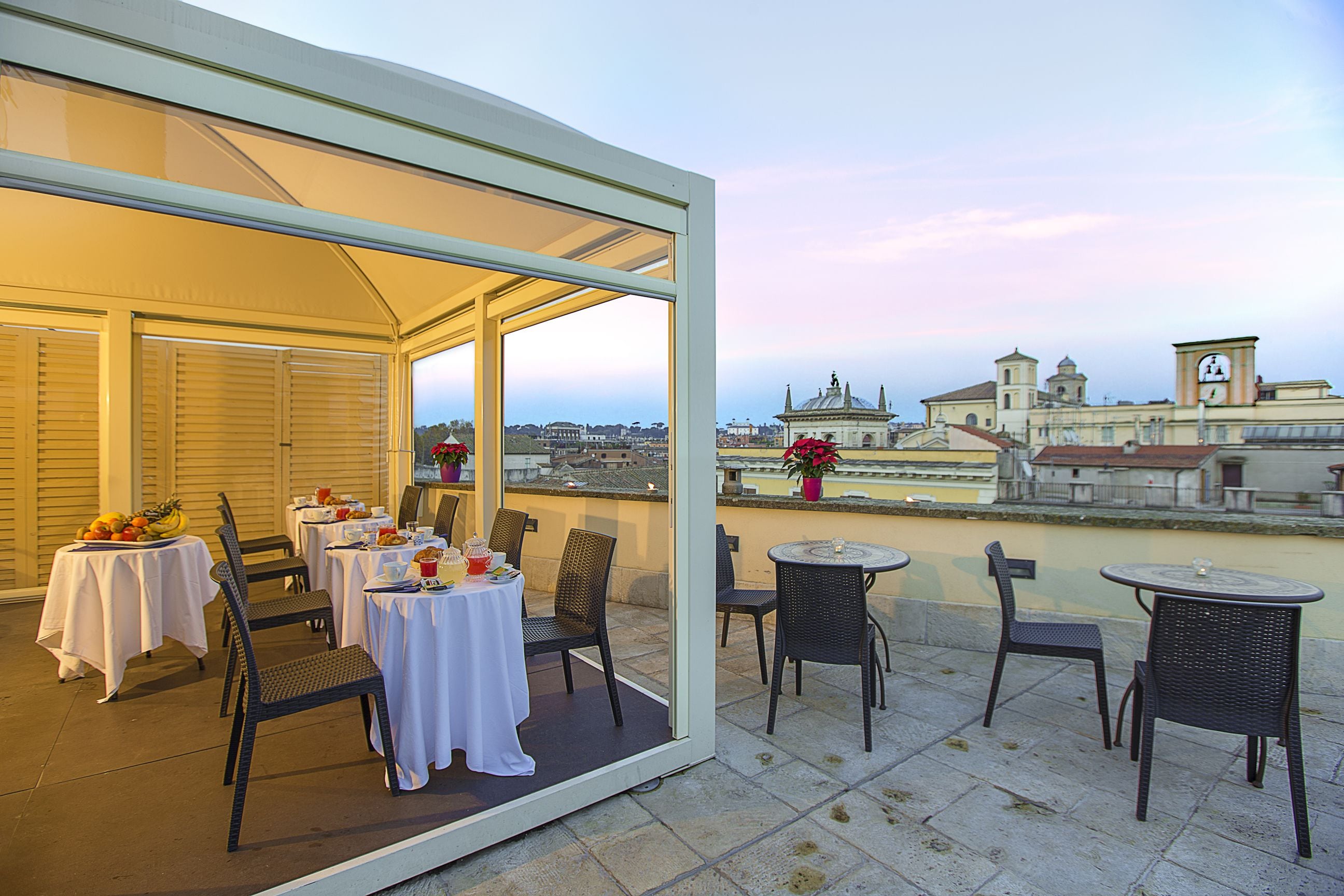 An outdoor terrace with tables and chairs, overlooking a cityscape with historical buildings.