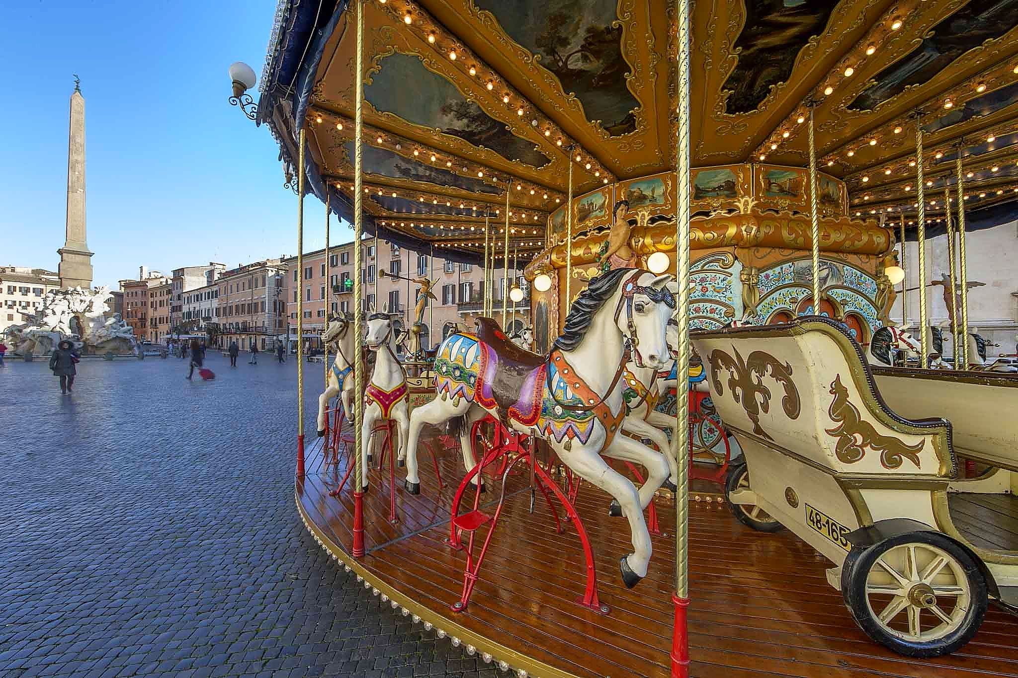 Un carrusel con elaboradas decoraciones doradas y caballos en una plaza pública.