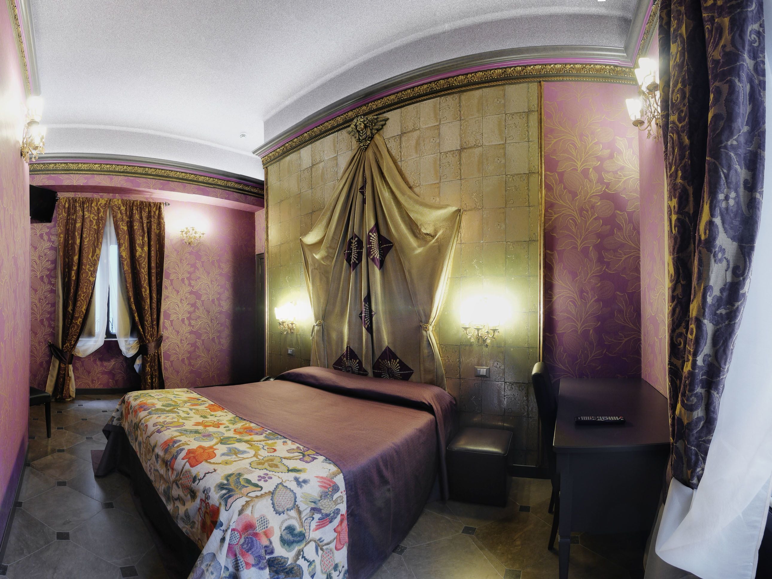 Une chambre d’hôtel avec un lit, un bureau et une chaise. Deux appliques murales assurent l’éclairage.
