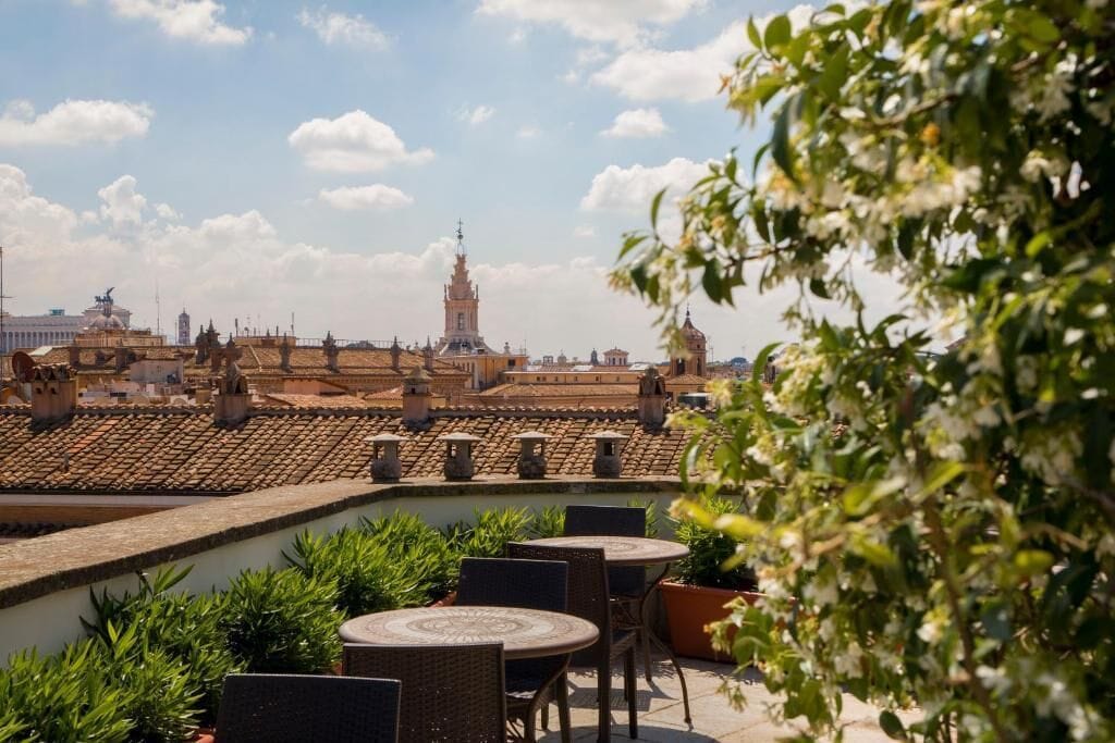 A rooftop terrace with outdoor seating, a view of historic buildings, and a clear sky.