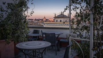 Um terraço com mesa e cadeiras, com vista para um edifício histórico com cúpula e arcos.